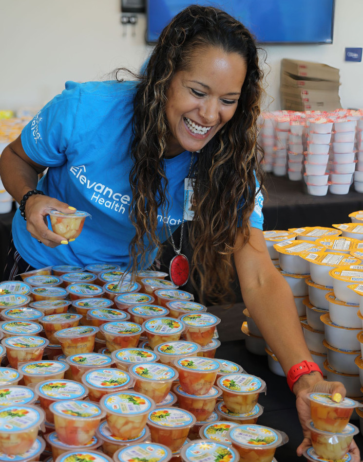 A woman smiling while stacking fruit cups for the Elevance Health Foundation.